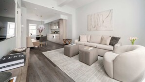 Un salon moderne avec un canapé, des poufs, une table basse et, au fond, un coin repas.