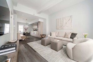 A modern living room with a sofa, ottomans, a coffee table, and a dining area in the background. - 17john: Luxury 3 Bed W/D in Unit + GYM + Lounge (New York)