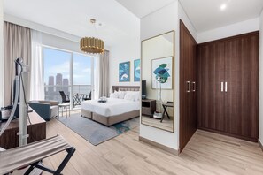 A hotel room with a large bed, a sitting area with a chair and a table, a large mirror, and a view of the city. - Stayshort - Dubai Media City Sleeps 2 With Amazing Sea Views (Dubai)