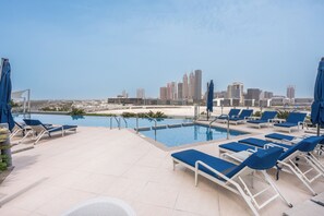 A rooftop pool area with lounge chairs and umbrellas, overlooking a city skyline. - Stayshort - Dubai Media City Sleeps 2 With Amazing Sea Views (Dubai)