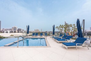 A rooftop pool with lounge chairs and umbrellas, overlooking a cityscape. - Stayshort - Dubai Media City Sleeps 2 With Amazing Sea Views (Dubai)