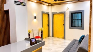 A hotel reception area with a check-in counter, two doors, a reception desk, a chair, and a sofa. - The Home Stay Golden Key (Varanasi)