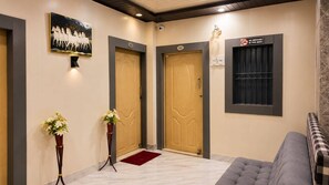 A hotel lobby with two wooden doors, a framed picture of horses, a no smoking sign, and a checkered sofa. - The Home Stay Golden Key (Varanasi)