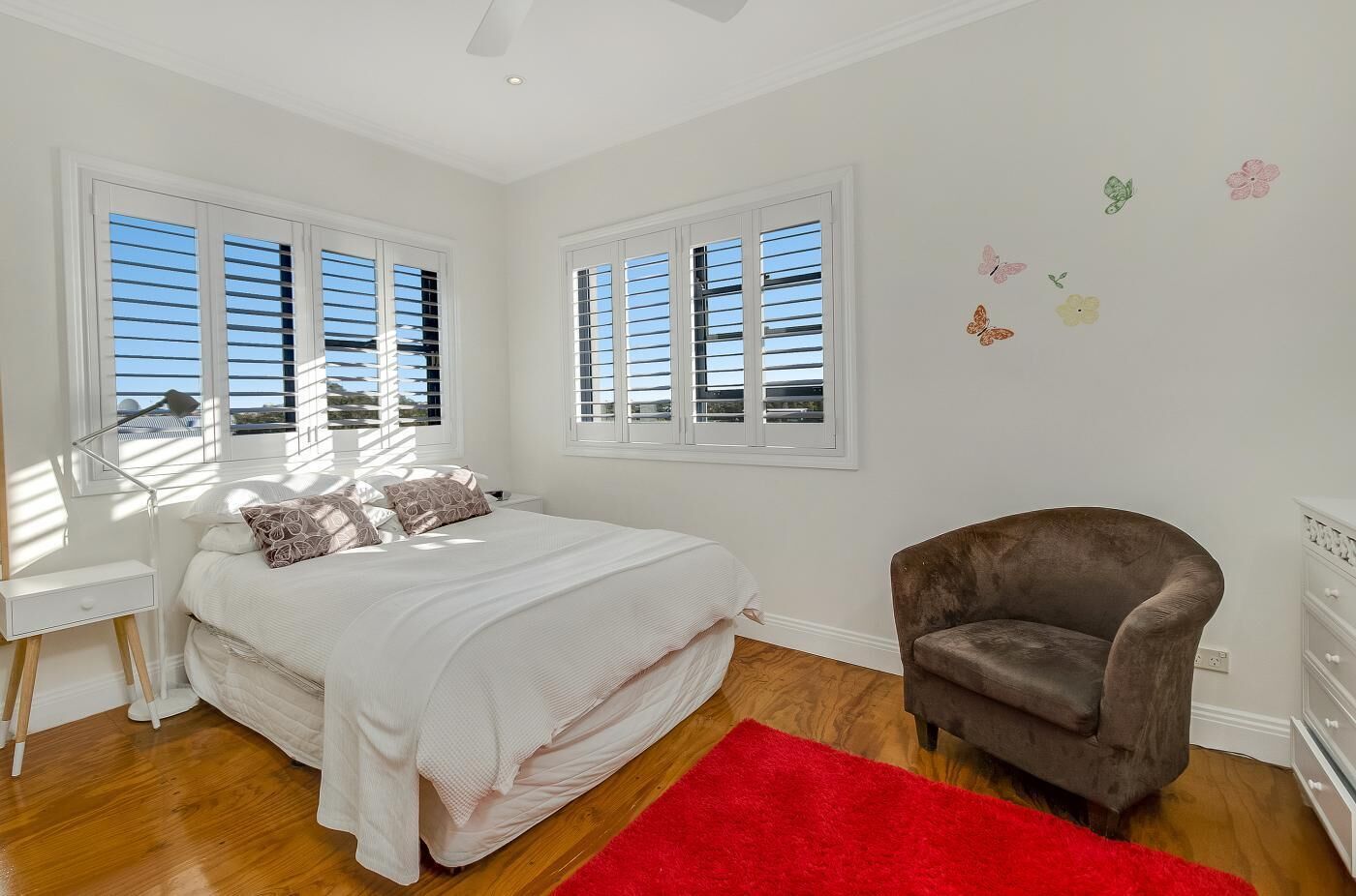 A bedroom with a bed, a desk, a chair, and a red rug.