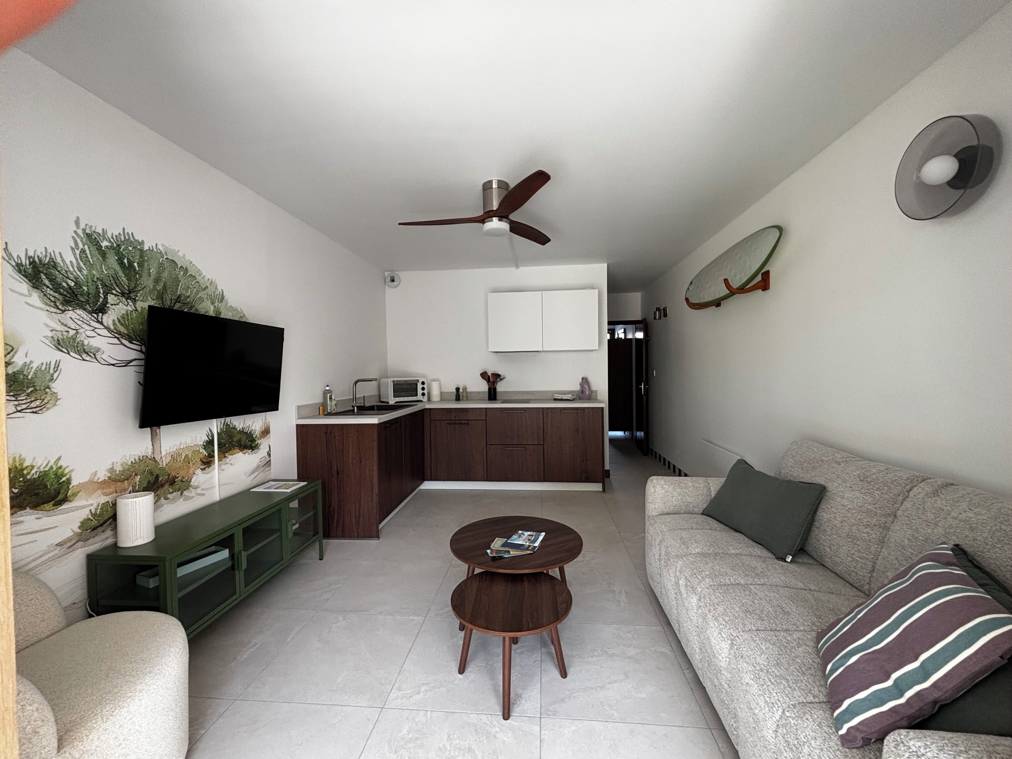 A modern living room with a flat-screen TV, a sofa, a coffee table, and a kitchen area with a microwave.