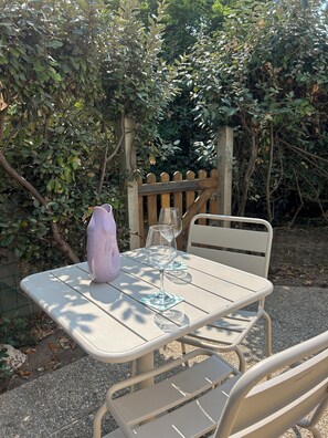 An outdoor table with a glass and a vase, set against a backdrop of greenery and a wooden fence. - Access to La Cotinière Beach—La Cabane de Philippine (Saint-Pierre-d'Oléron)