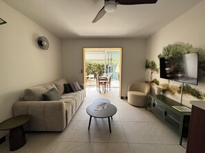 A living room with a sofa, coffee table, TV, and a view of the outdoors. - Access to La Cotinière Beach – La Cabane de Philippine (Saint-Pierre-d'Oléron)