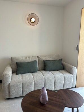 A living room with a sofa, a round coffee table, and a wall-mounted light fixture. - Access to La Cotinière Beach—La Cabane de Philippine (Saint-Pierre-d'Oléron)