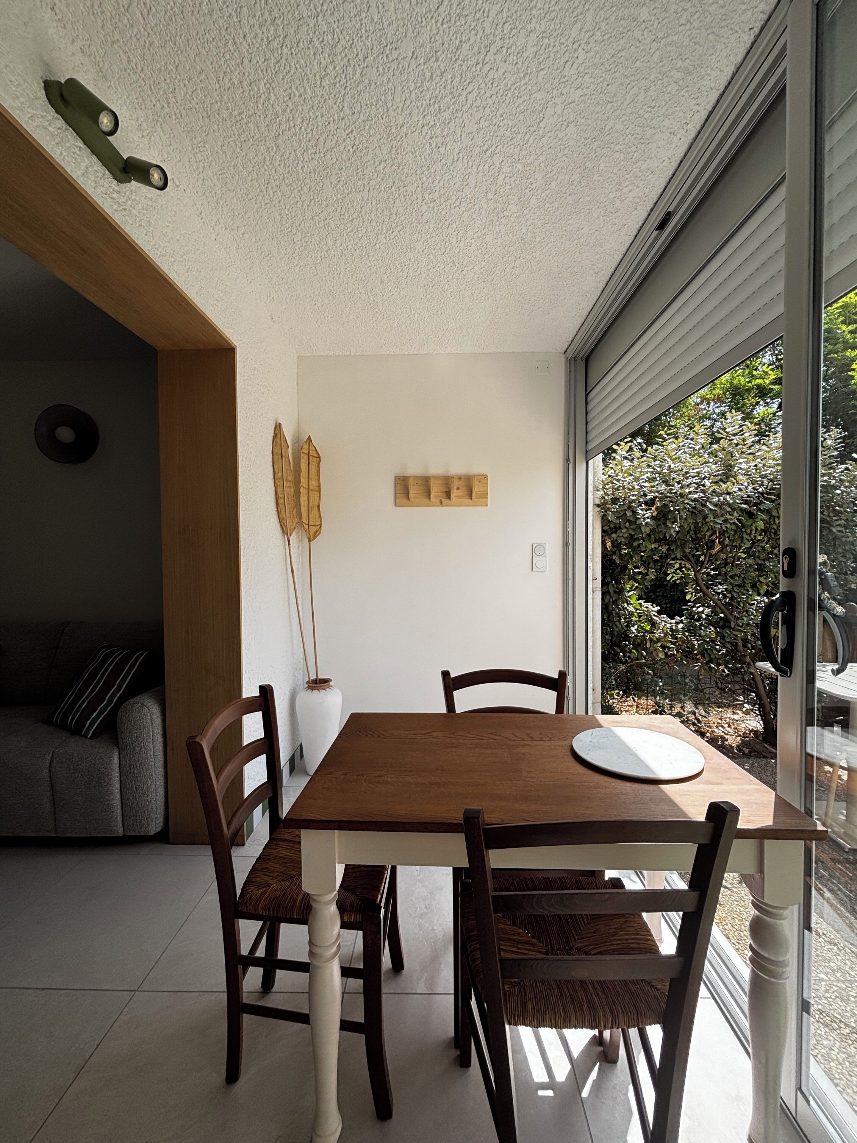 Un coin repas avec une table et des chaises en bois, un vase et un luminaire fixé au mur.
