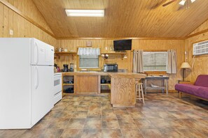 A compact kitchen with a refrigerator, stove, microwave, and a small dining area with a table and a couch. - Casita: 1  BR, 1  BA House in Concan, Sleeps 4 (Concan)