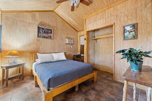 A wooden-paneled bedroom with a bed, a nightstand, a lamp, a wall-mounted heater, and a potted plant. - Casita: 1  BR, 1  BA House in Concan, Sleeps 4 (Concan)