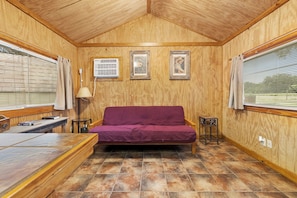 A cozy room with a wooden ceiling, a purple sofa, a small table, and two framed pictures on the wall. - Casita: 1  BR, 1  BA House in Concan, Sleeps 4 (Concan)