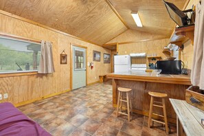 Une cuisine compacte avec un îlot central, des tabourets en bois et une fenêtre équipée de stores.