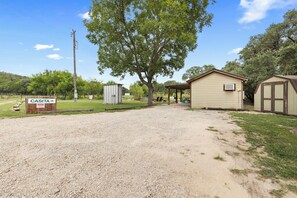 A gravel parking area leading to a building with a covered picnic area and a small shed. - Casita: 1  BR, 1  BA House in Concan, Sleeps 4 (Concan)