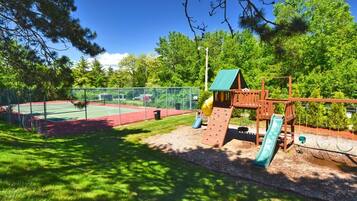 Un parque infantil con tobogán, pared de escalada y cancha de tenis.