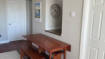 Una habitación con una mesa de madera y bancos, un reloj en la pared y una puerta.