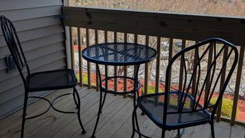 Terraza de madera con una mesa metálica y dos sillas, con vista a un lago y árboles.