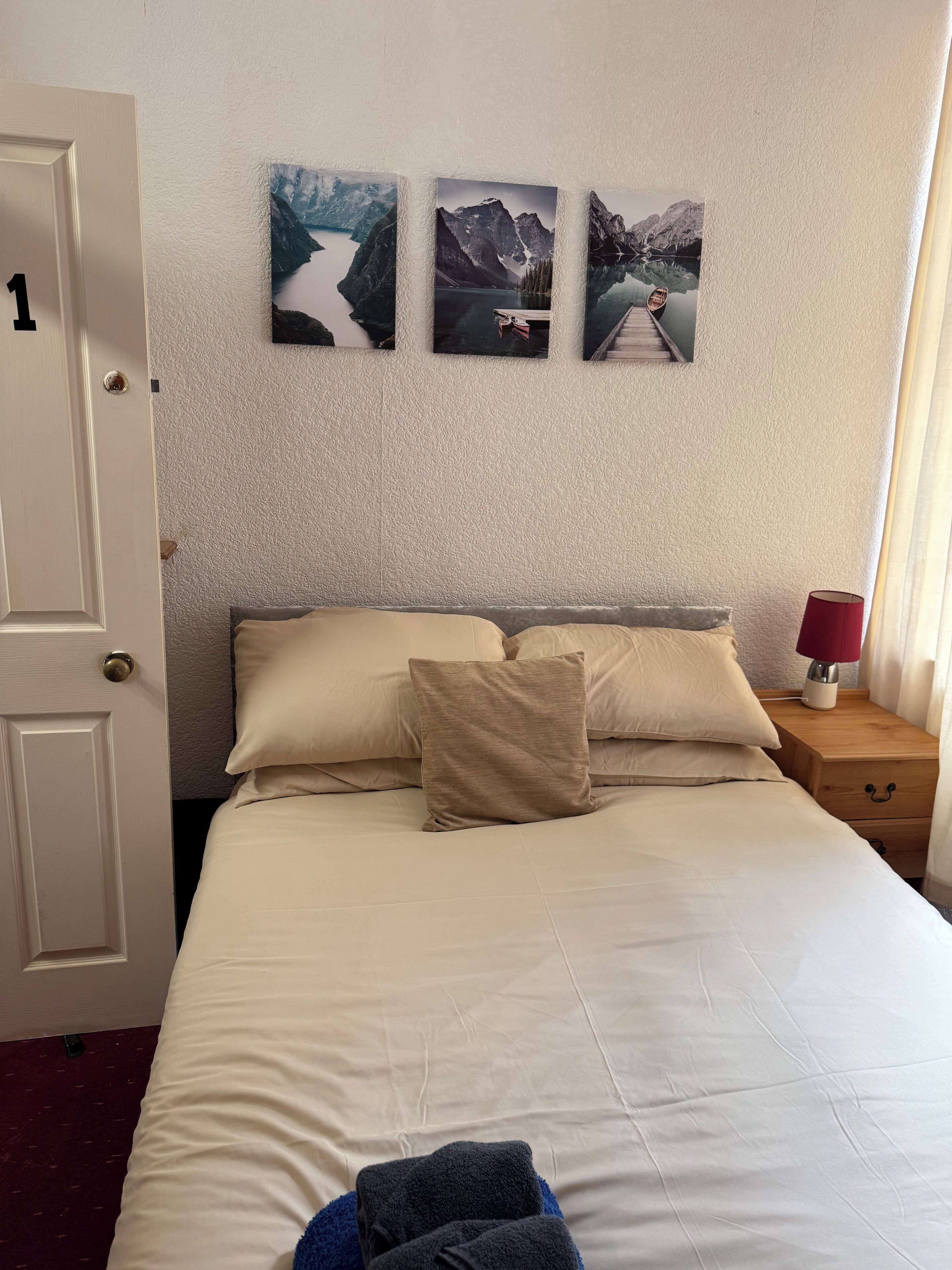 Habitación de hotel con una cama, una mesita de noche con lámpara y tres cuadros en la pared.