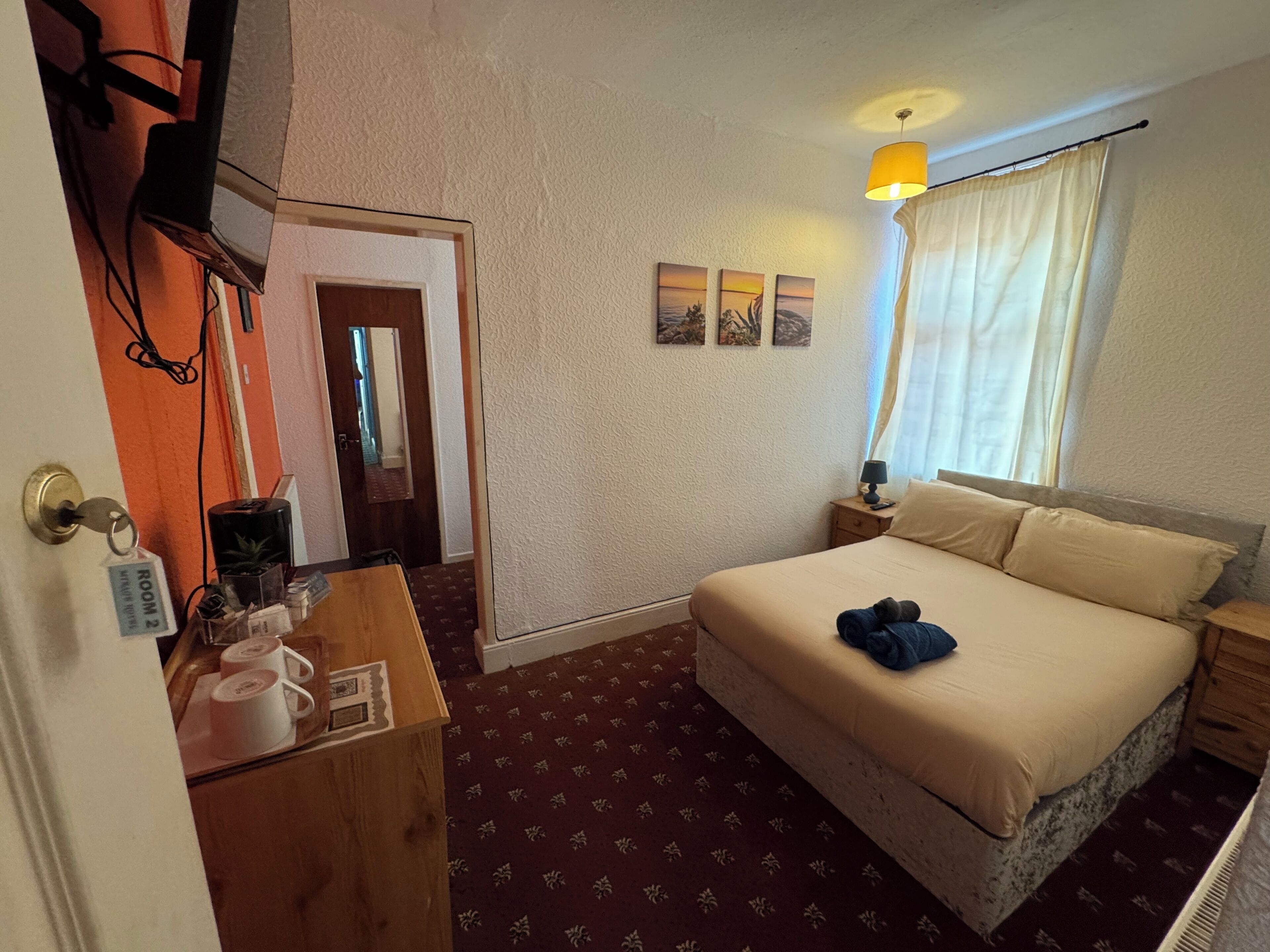 Una habitación de hotel con cama, escritorio, teléfono, lámpara y ventana con cortinas.