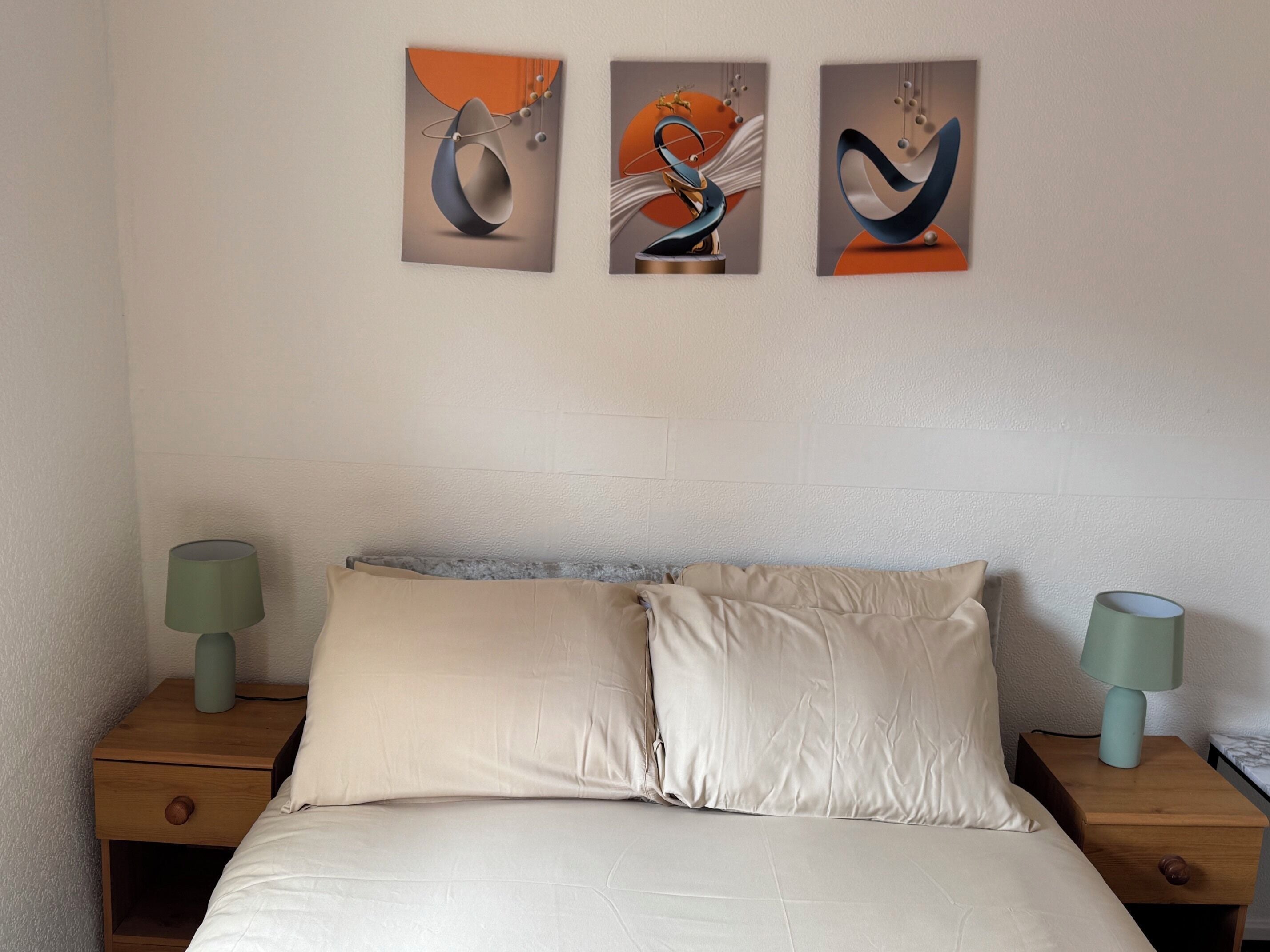 Une chambre à coucher avec un lit, deux tables de chevet et trois tableaux abstraits accrochés au mur.