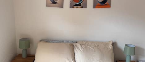 Un dormitorio con una cama, dos mesitas de noche y tres cuadros abstractos en la pared.