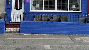 Un hotel llamado 'MIRAGE' con fachada azul, ventanas grandes y un cartel que indica habitaciones disponibles.