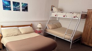 Una habitación con una cama individual, una litera, una mesita de noche con lámpara y un armario de madera.