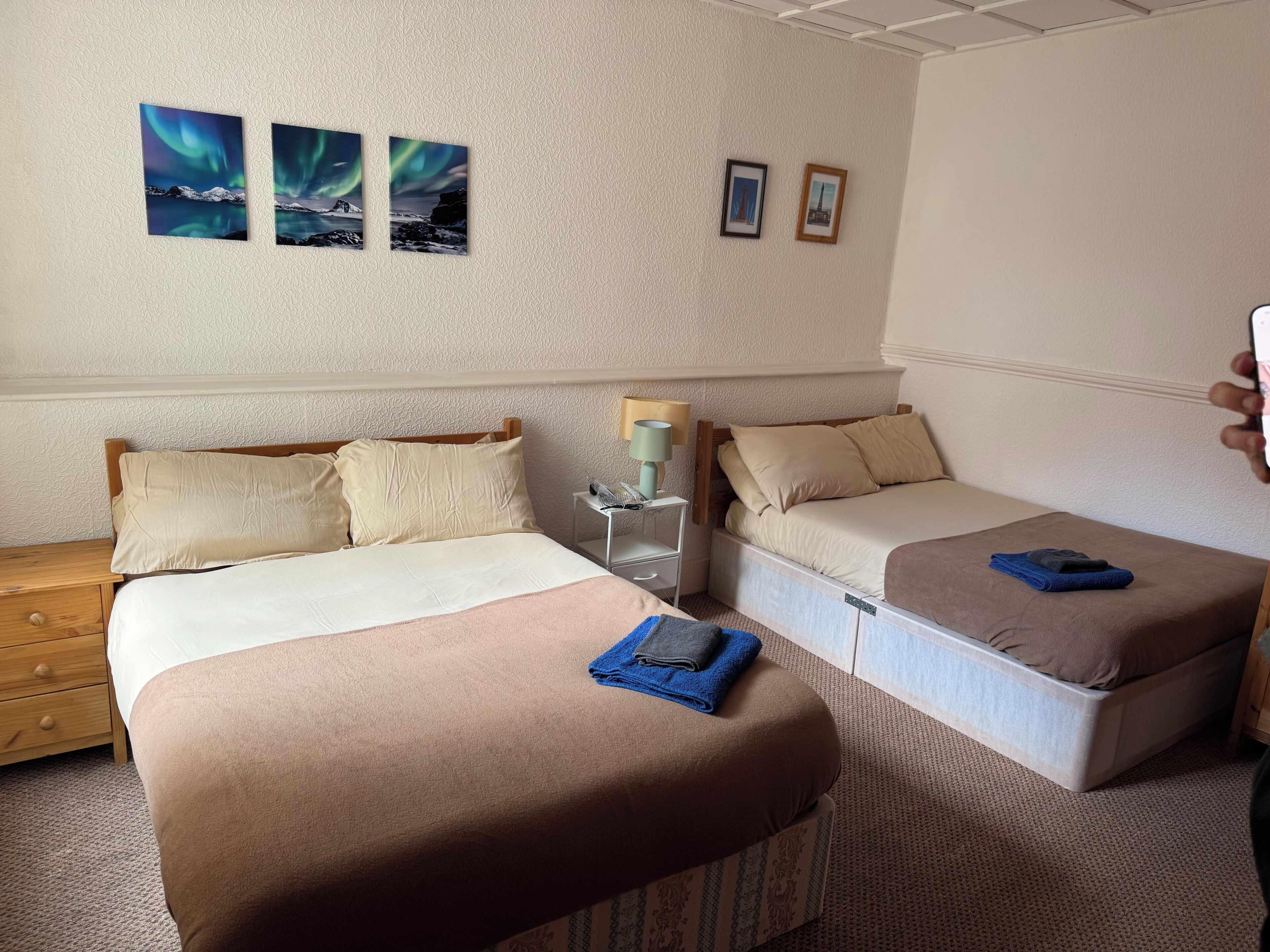 A hotel room with two beds, a nightstand, a lamp, and wall art.