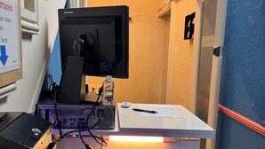 Mostrador de recepción con un monitor, una botella de agua y un cartel que indica la zona de recepción.