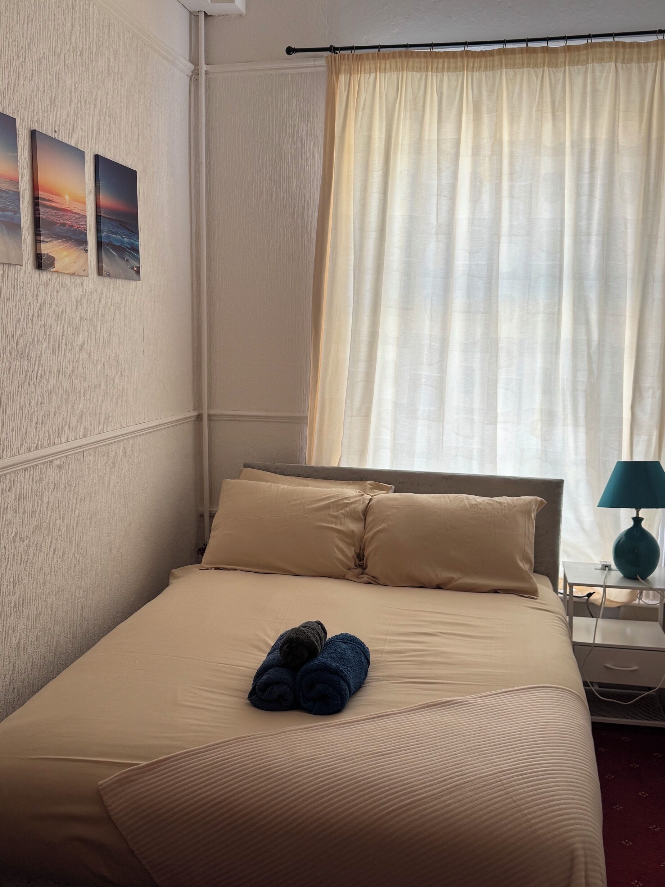 A hotel room with a bed, pillows, a nightstand with a lamp, and a window with curtains.