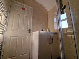 Une salle de bain avec une douche, un lavabo et une porte dotée d’une poignée.