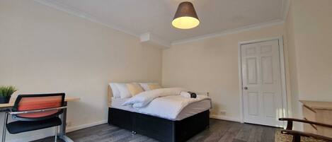 A bedroom with a bed, a desk, a chair, and a door.