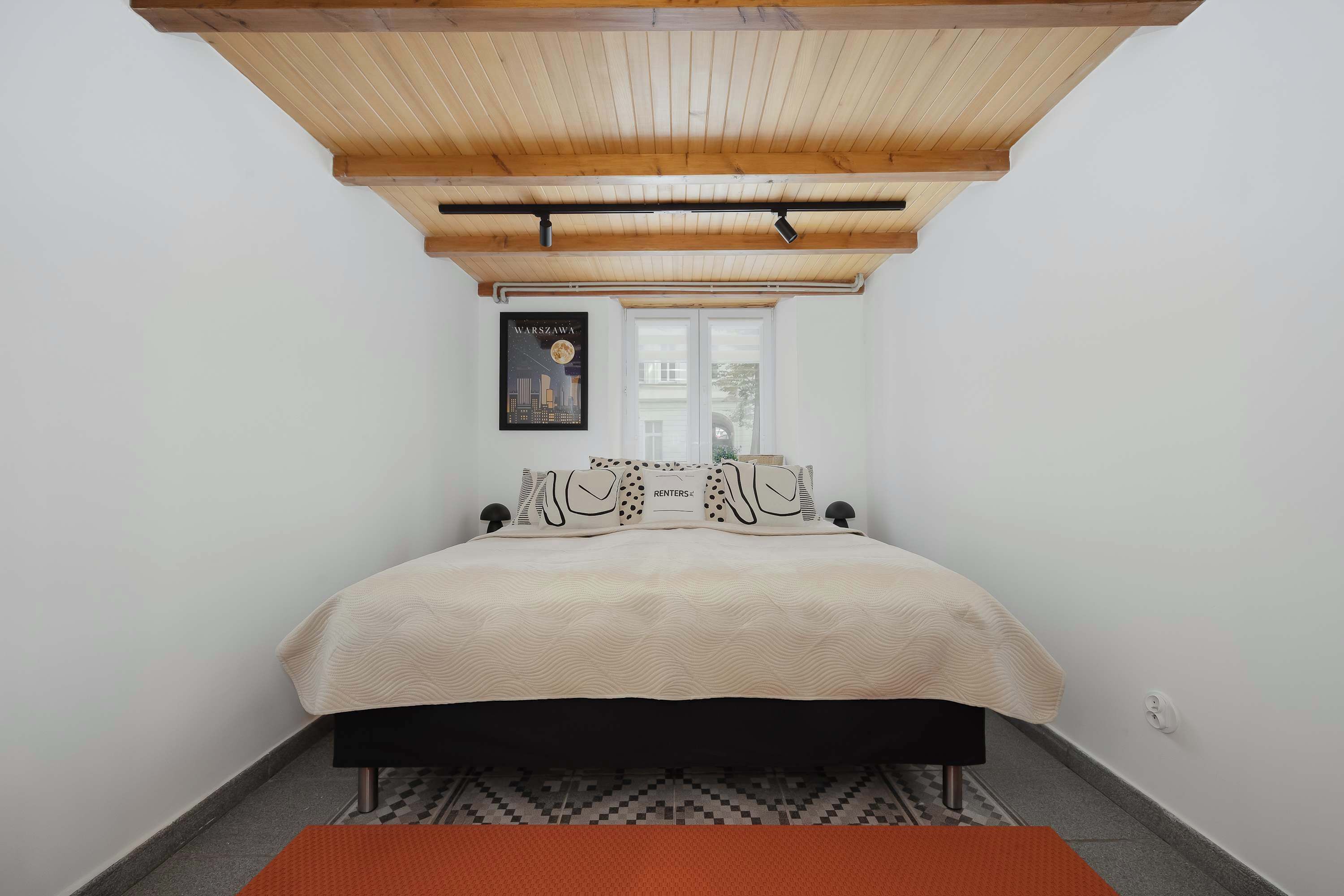Une chambre à coucher avec un lit, une fenêtre, un tableau encadré au mur et un plafond avec des poutres en bois.