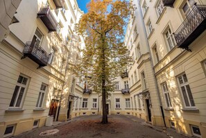 Ein von Bäumen gesäumter Innenhof mit Gebäuden an beiden Seiten, inklusive Balkonen und Fenstern.