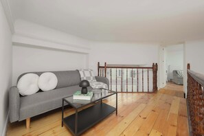 A modern living room with a grey sofa, a glass coffee table, and a view of a balcony with wooden railings. - Charming Flat with a Mezzanine | 2 Bedrooms | Close to the City Centre (Warszawa)