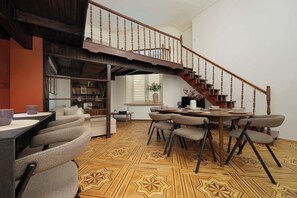 A dining area with a wooden staircase leading to an upper level, a round table with chairs, and a patterned floor. - Charming Flat with a Mezzanine | 2 Bedrooms | Close to the City Centre (Warszawa)