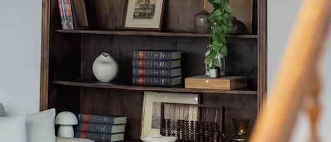Una estantería de madera con libros, un florero y un cuadro enmarco.