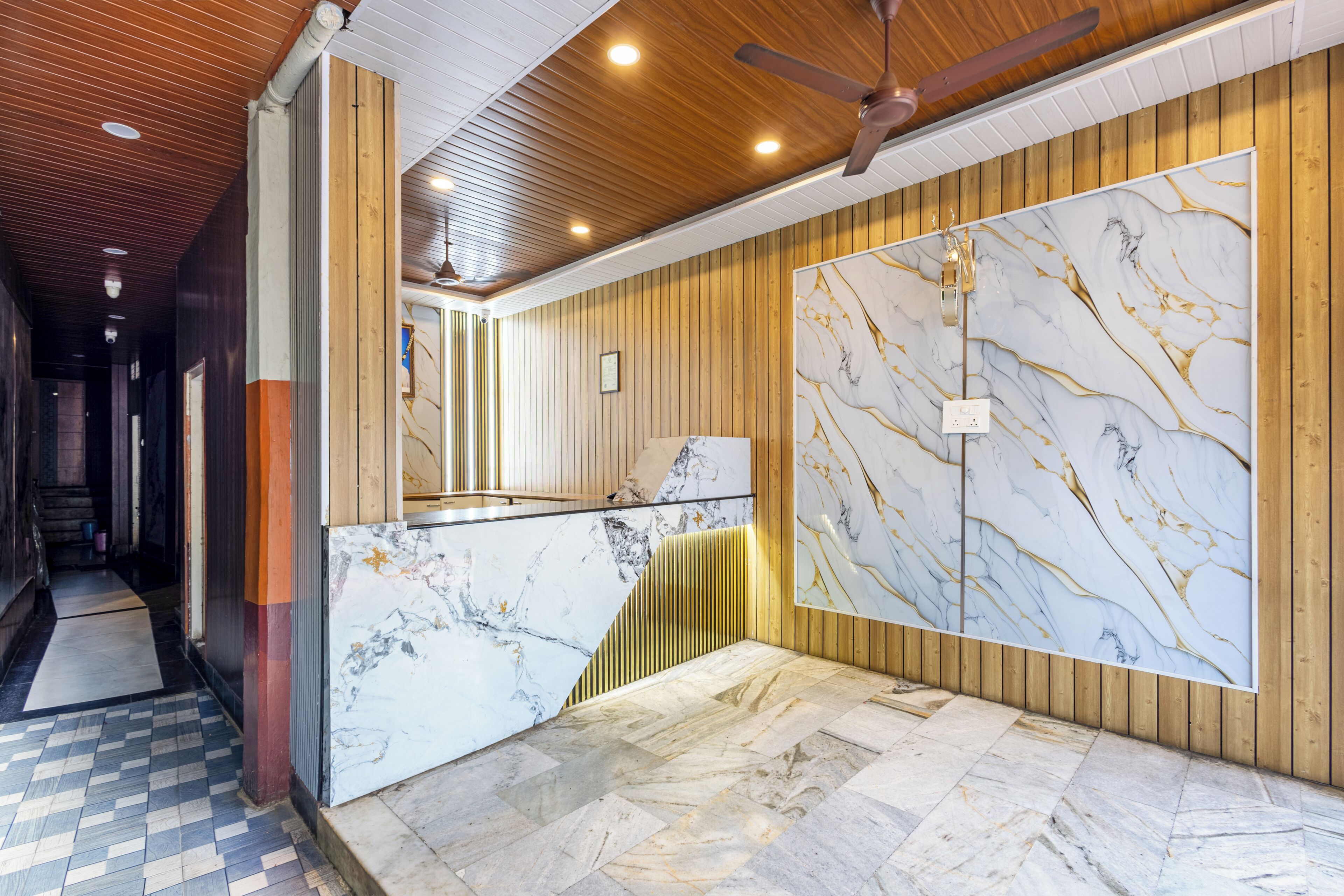 Un vestíbulo de hotel con mostrador de recepción de mármol, paneles de madera y un ventilador de techo.