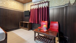 A hotel room with a wooden ceiling, a bed, a small table with a lamp, a red chair, and a wall-mounted air conditioner. - Srinivasa Residency - SVGMC (Tirupati)