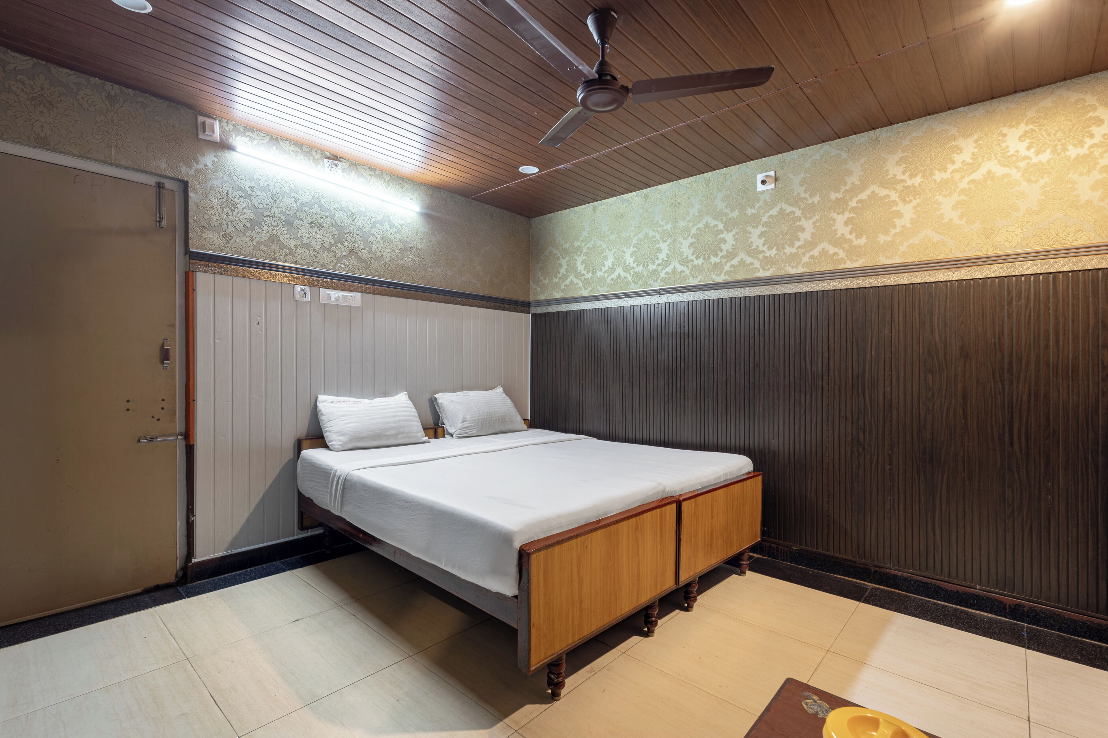 A bedroom with a bed, a wardrobe, a ceiling fan, and a patterned wall.