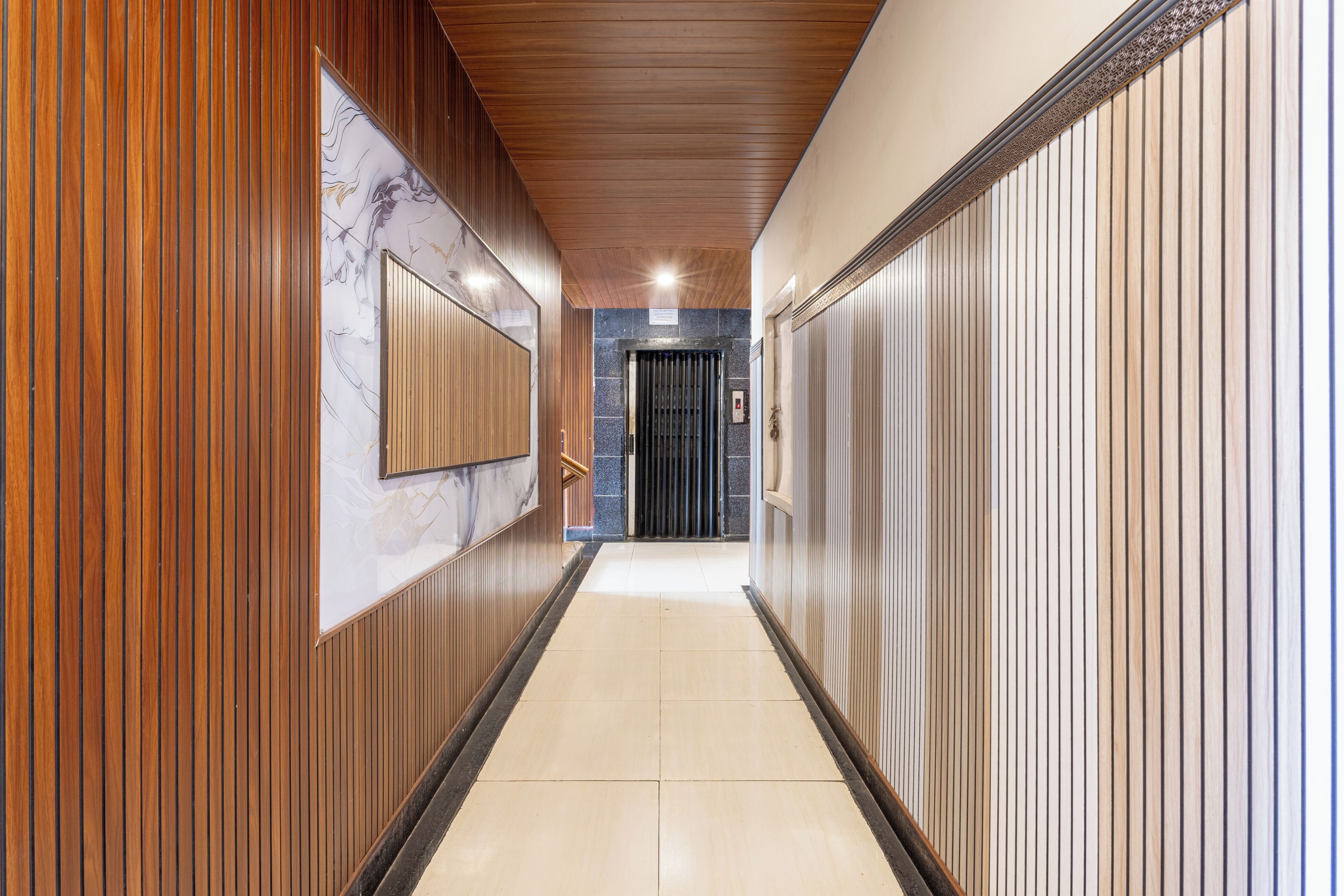 Un pasillo con paneles de madera en las paredes, un muro de mármol con un diseño decorativo y suelo de baldosas.