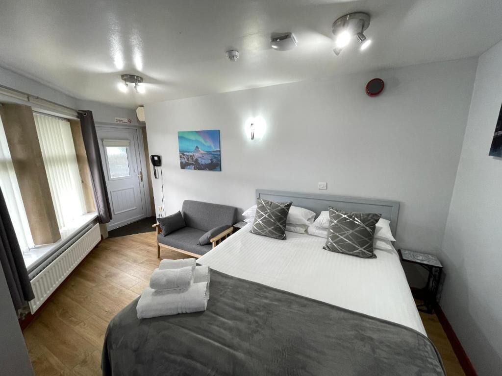 A hotel room with a bed, a chair, a window, and a painting on the wall.