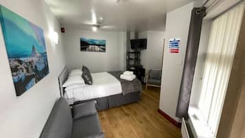 A hotel room with a bed, a sofa, a TV, and a window with blinds.