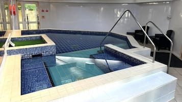 An indoor swimming pool with a blue tiled floor, a small grassy area, and a seating area with chairs and a table.