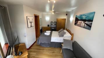 Un dormitorio con cama, sofá, escritorio, televisor y obras de arte en las paredes.
