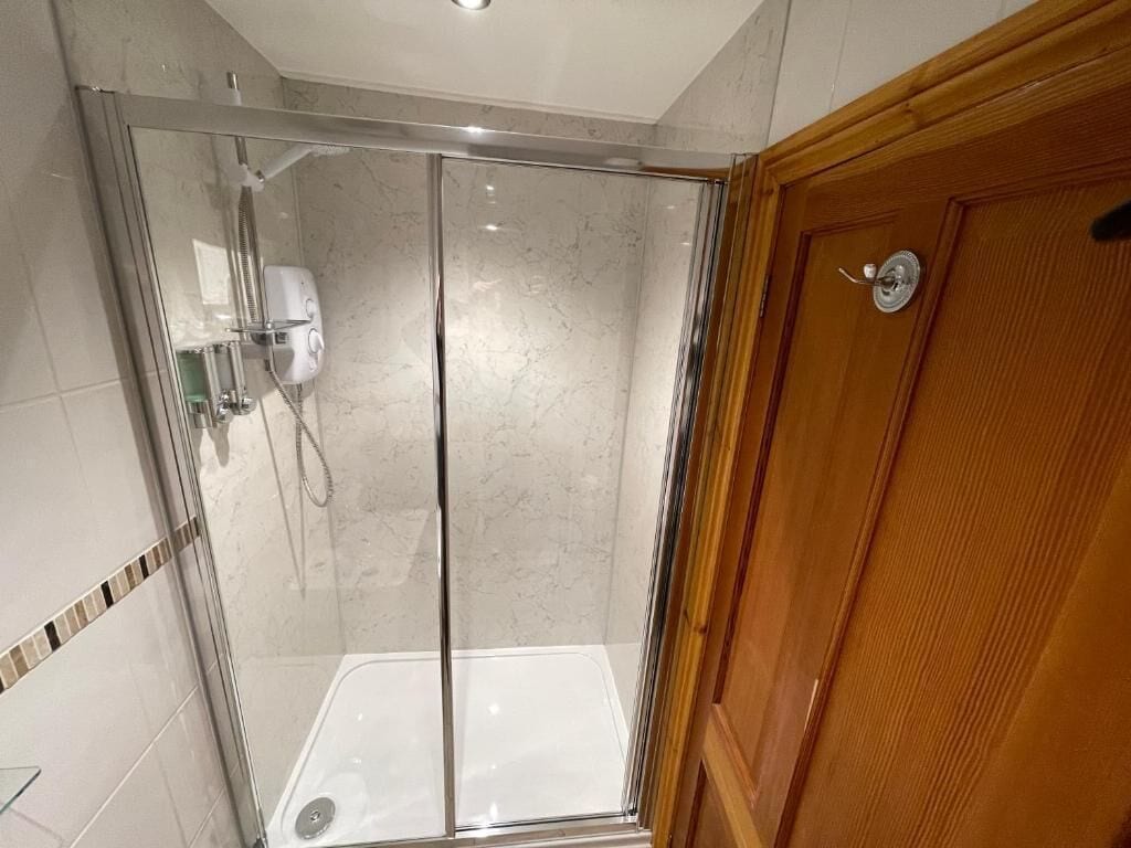 A glass-enclosed shower with a wooden door and a tiled floor.