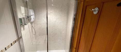 A glass-enclosed shower with a wooden door and a tiled floor.
