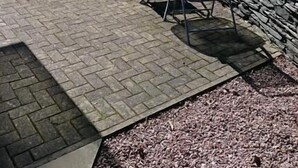 Un espacio al aire libre con mesas y sillas, un muro de piedra y suelo adoquinado.