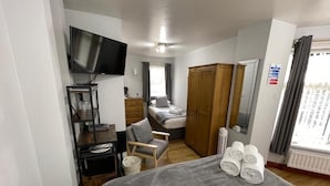 Habitación de hotel con cama, televisor, escritorio, silla, armario y ventana con cortinas.