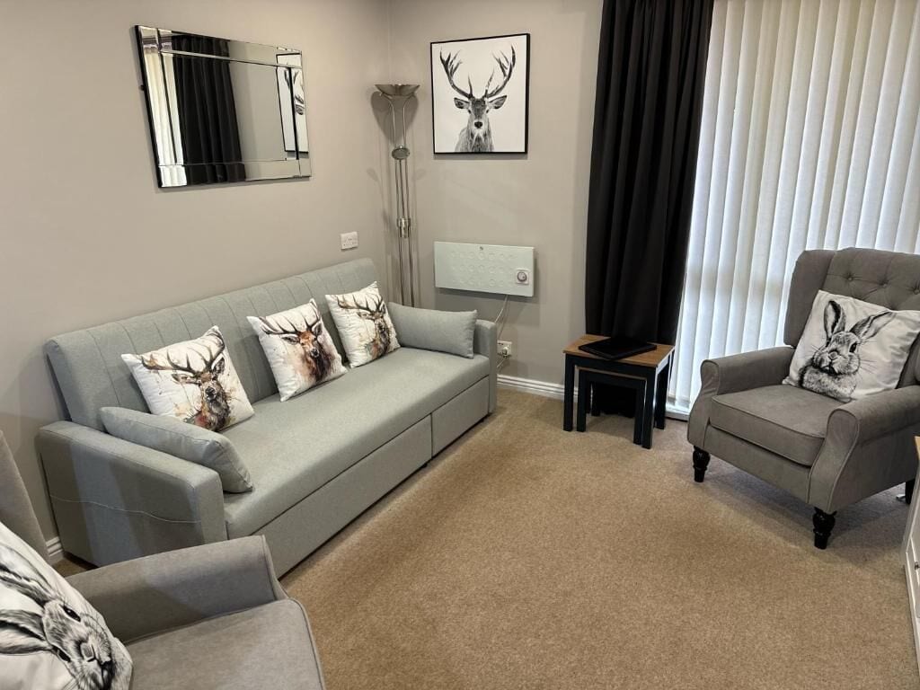 Un salon avec un canapé gris, un fauteuil gris et une petite table. Deux cadres avec des motifs d’animaux sont accrochés au mur.